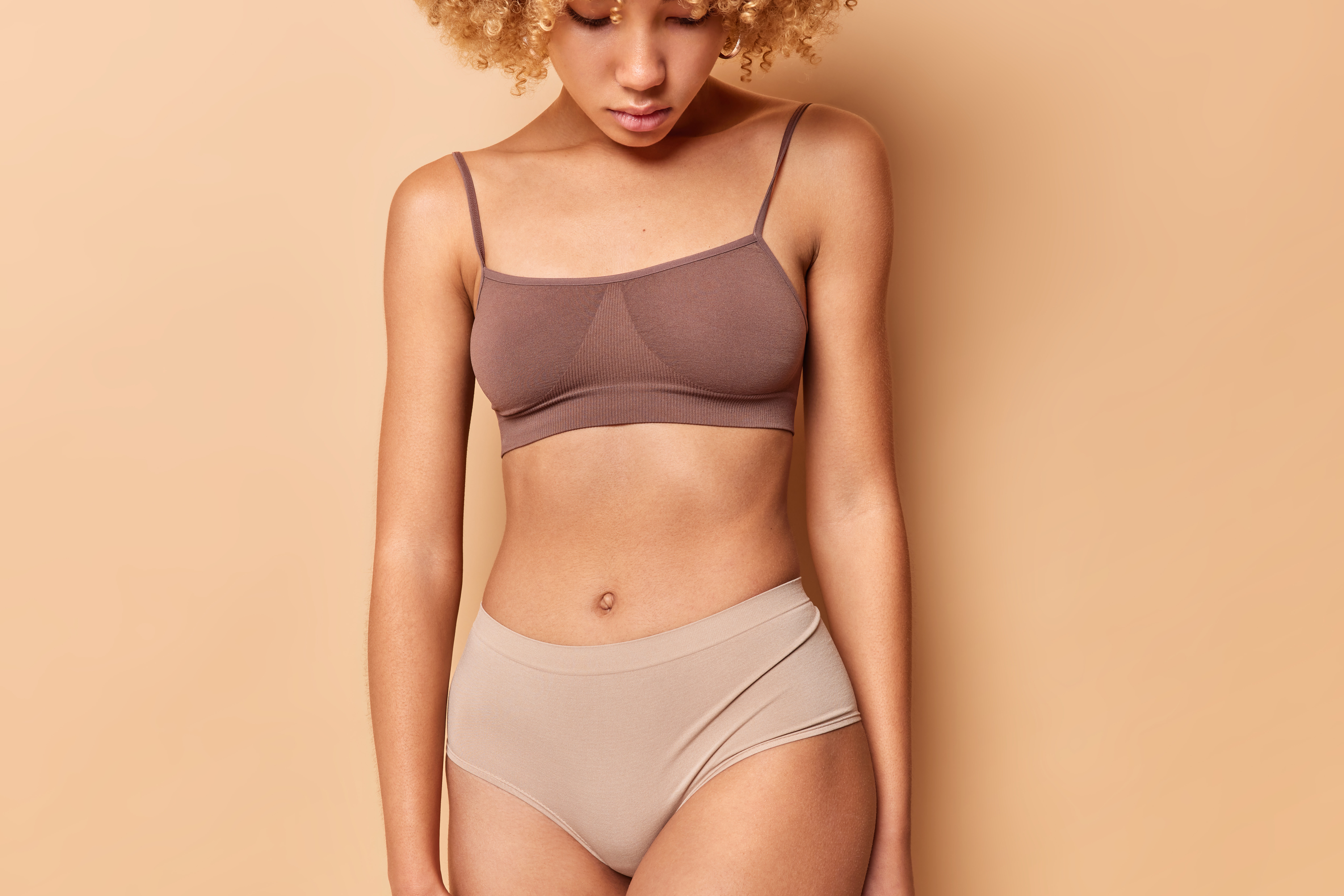 Cropped shot unrecognizable woman wears top panties has perfect body shape shows abdomen after liposuction isolated beige background ideal figure slimming concept torso fit female