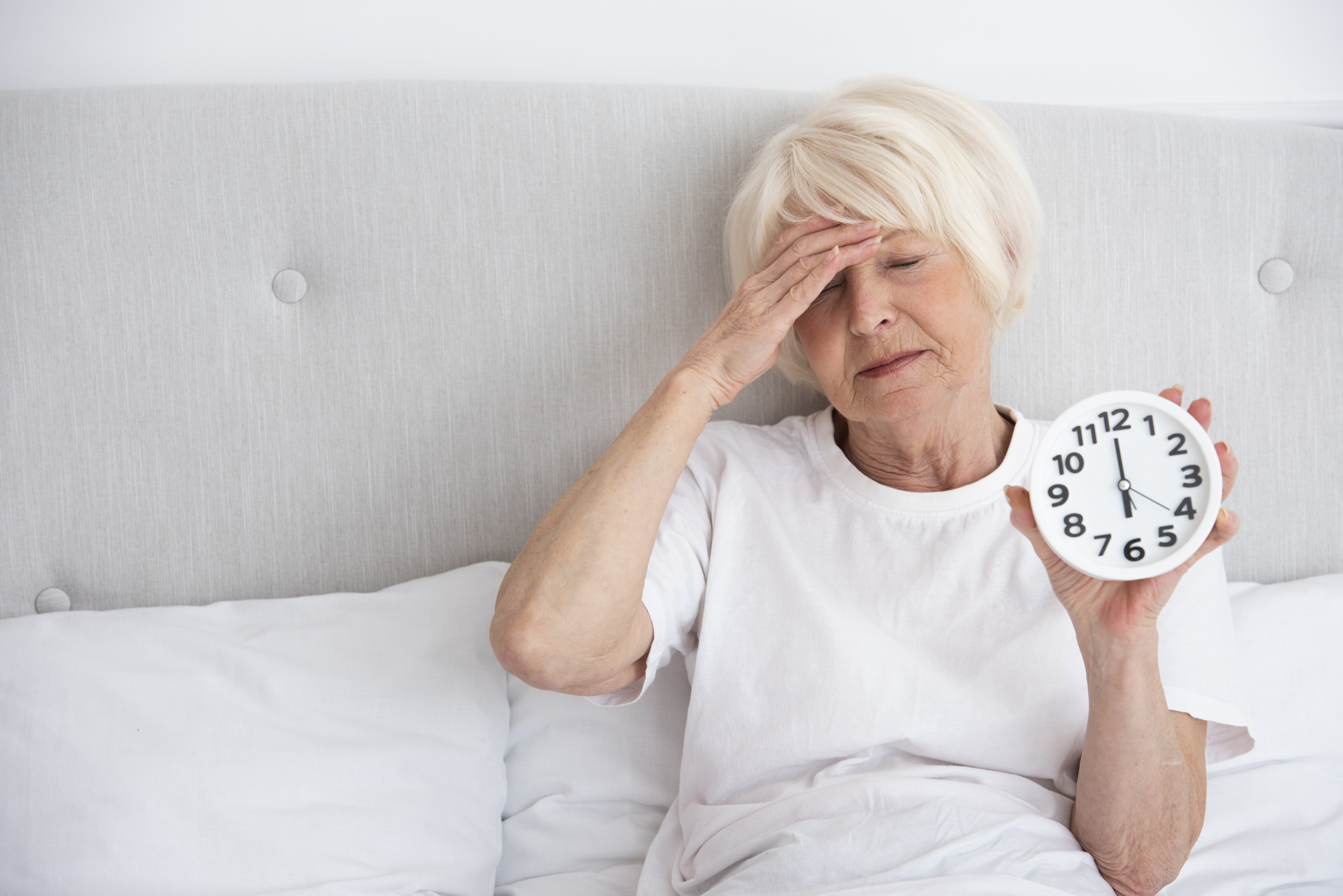 Elder woman holding clock her bed